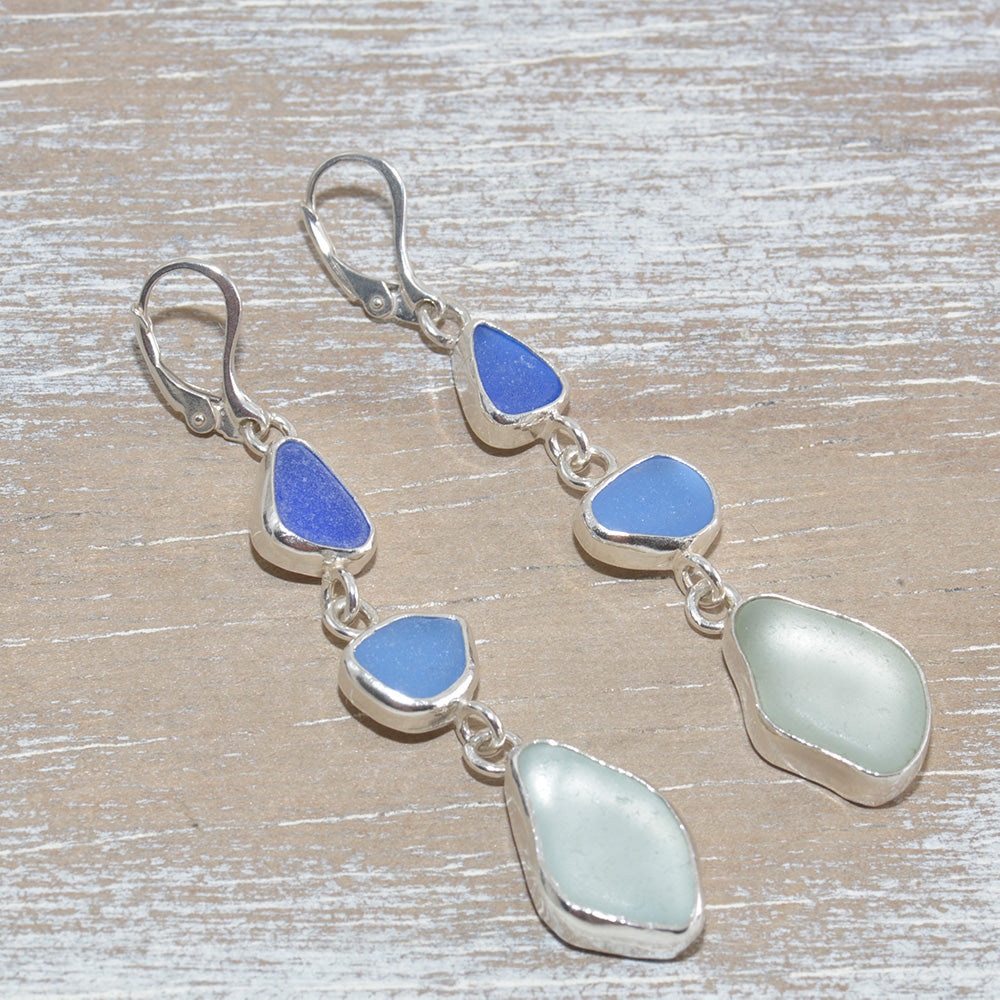 Sea glass dangle earrings in shades of blue in hand crafted settings of sterling silver. (E615)