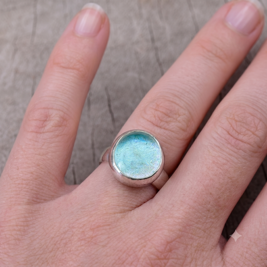 Hand wearing a ring with a blue gemstone on a neutral background