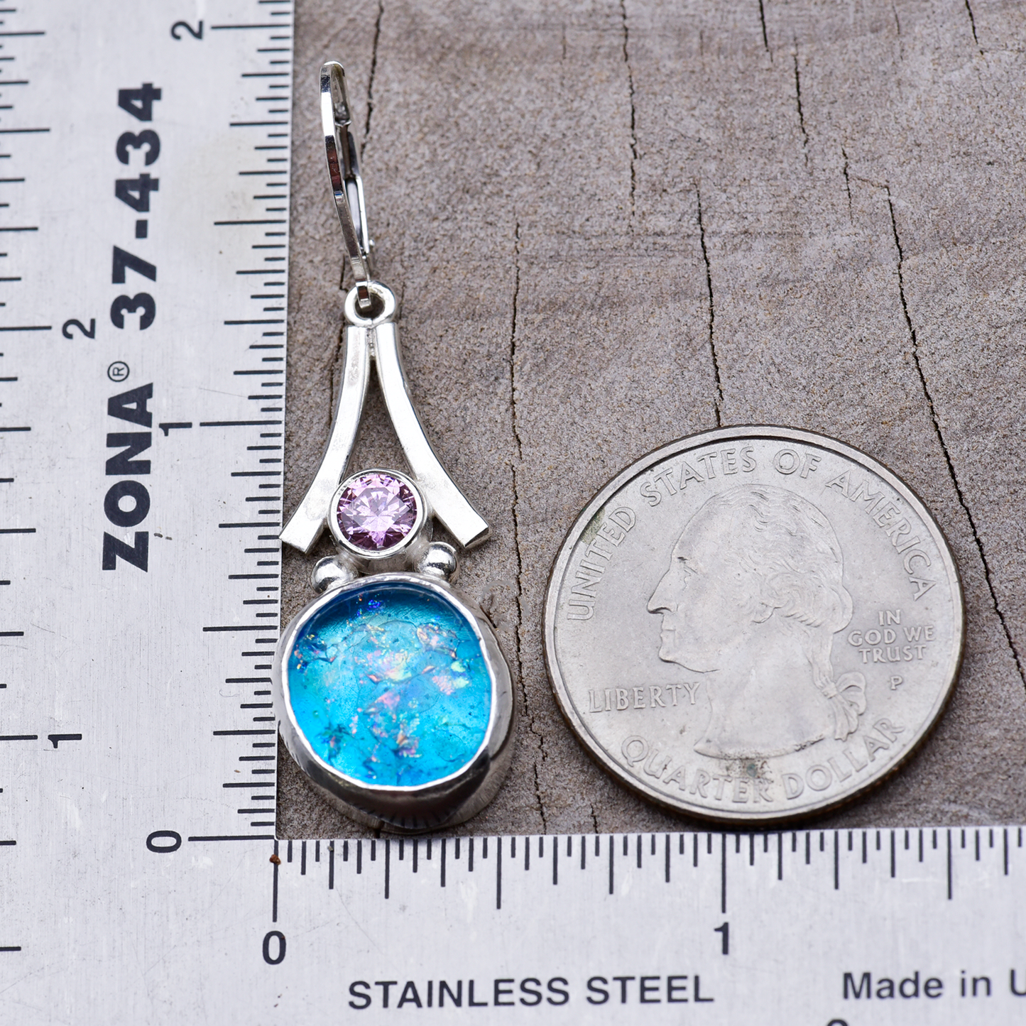 Turquoise dichroic glass drop earring beside a ruler and a quarter, measuring about 1¾ inches from ear wire to bottom