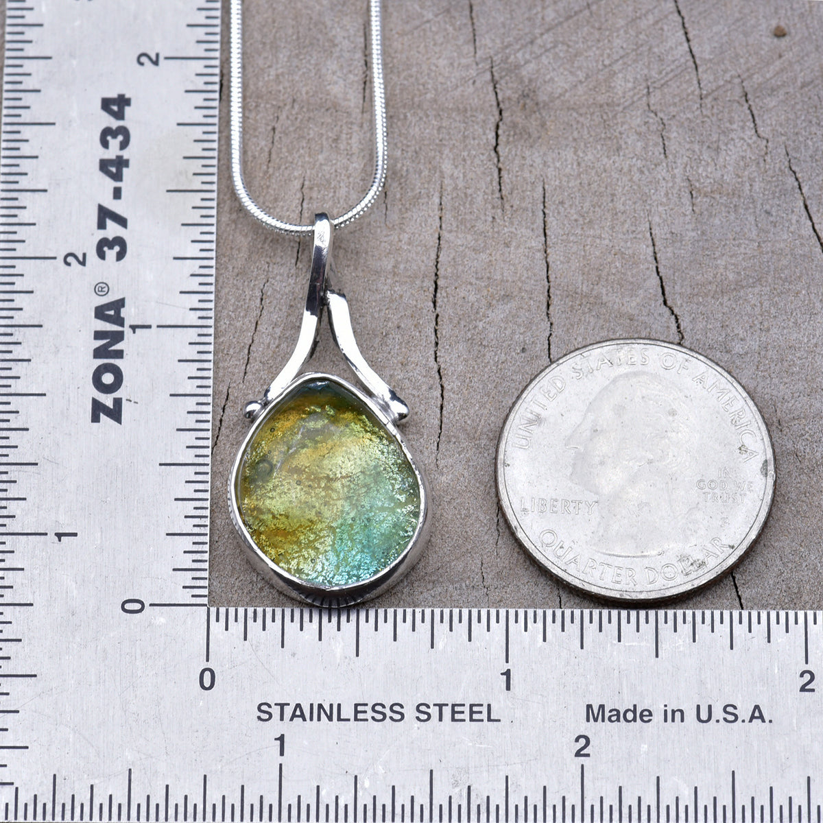Gold and aqua teardrop dichroic glass pendant beside a ruler and quarter, about 1½ inches long including the bail