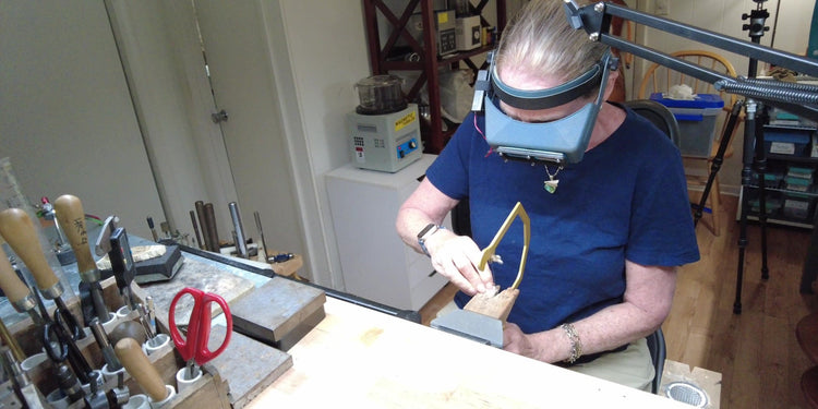 Sawing silver at the studio bench, with hand tools racked in the foreground.