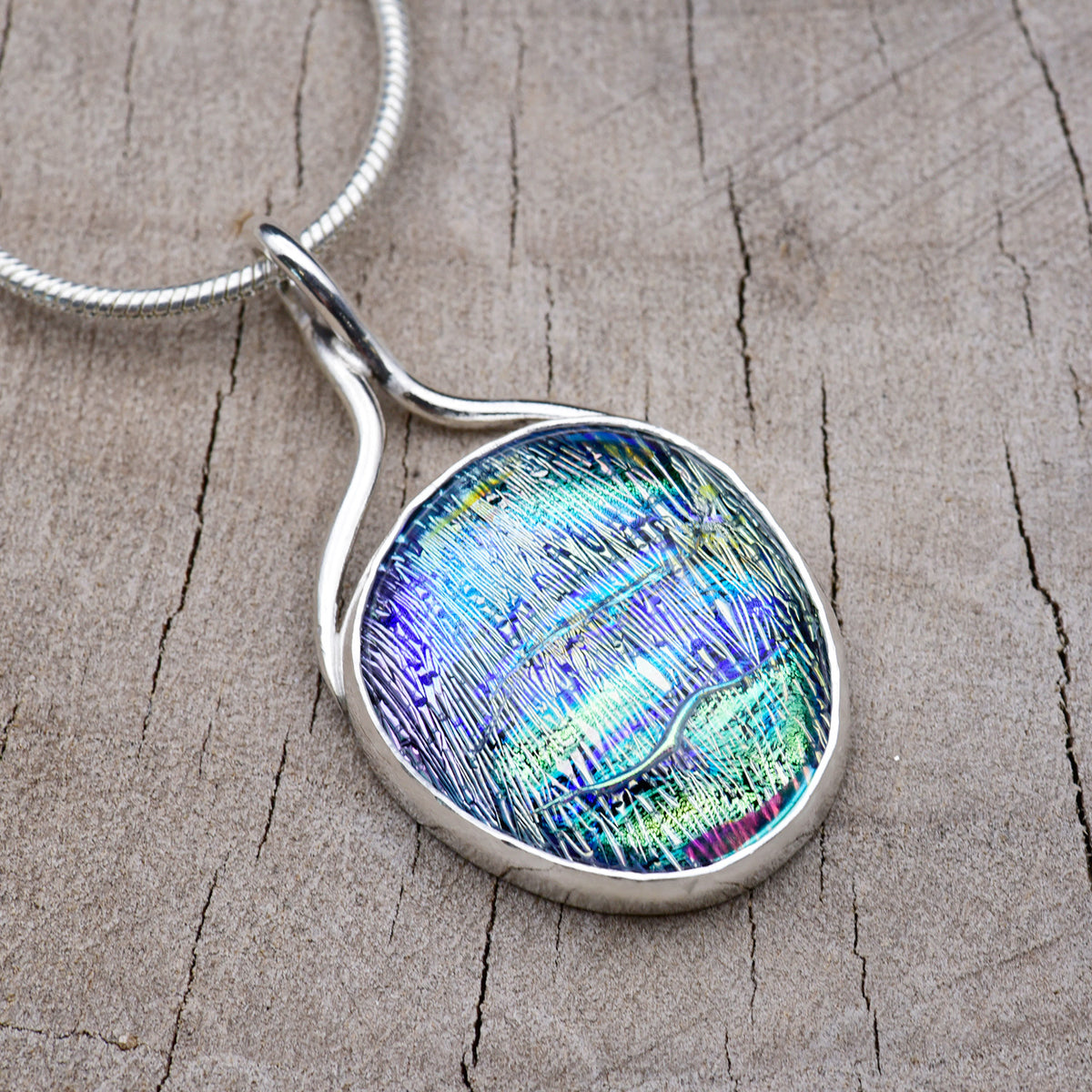 Handmade pendant necklace with an aqua and violet dichroic glass cabochon streaked with lime green and magenta, in an Argentium sterling silver setting with a ribbon bail, on a silver snake chain.