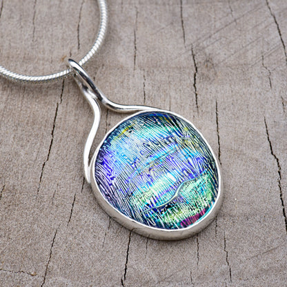 Handmade pendant necklace with an aqua and violet dichroic glass cabochon streaked with lime green and magenta, in an Argentium sterling silver setting with a ribbon bail, on a silver snake chain.