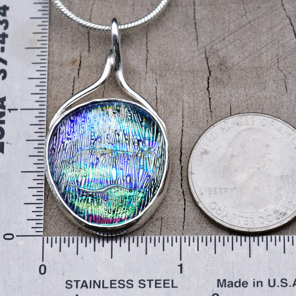 Aqua and violet dichroic glass pendant beside a ruler and a quarter for scale, about 1¾ inches long and 1 inch wide.