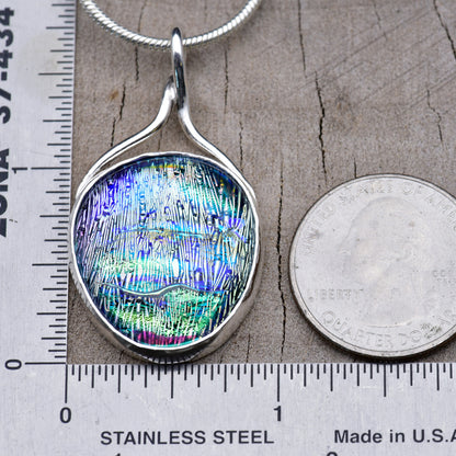 Aqua and violet dichroic glass pendant beside a ruler and a quarter for scale, about 1¾ inches long and 1 inch wide.