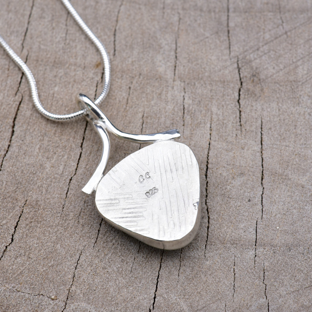 Back of the shield-shaped pendant showing the embossed linear texture with the CC maker's mark and 925 sterling silver hallmark.