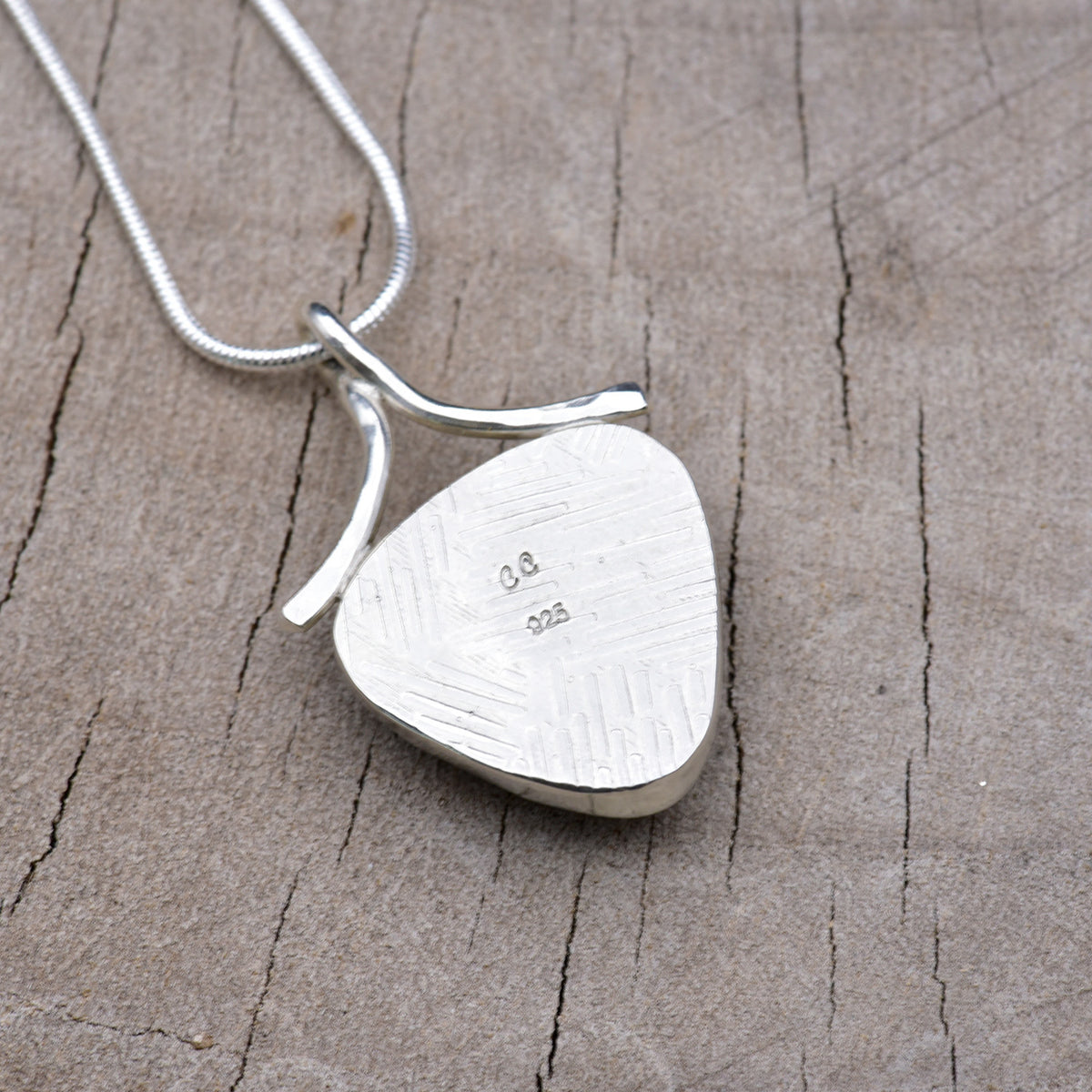 Back of the shield-shaped pendant showing the embossed crosshatch texture with the CC maker's mark and 925 sterling silver hallmark.