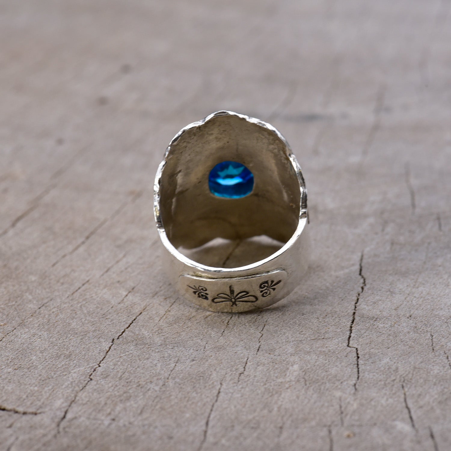 Back of silver ring with a blue gemstone on a wooden surface