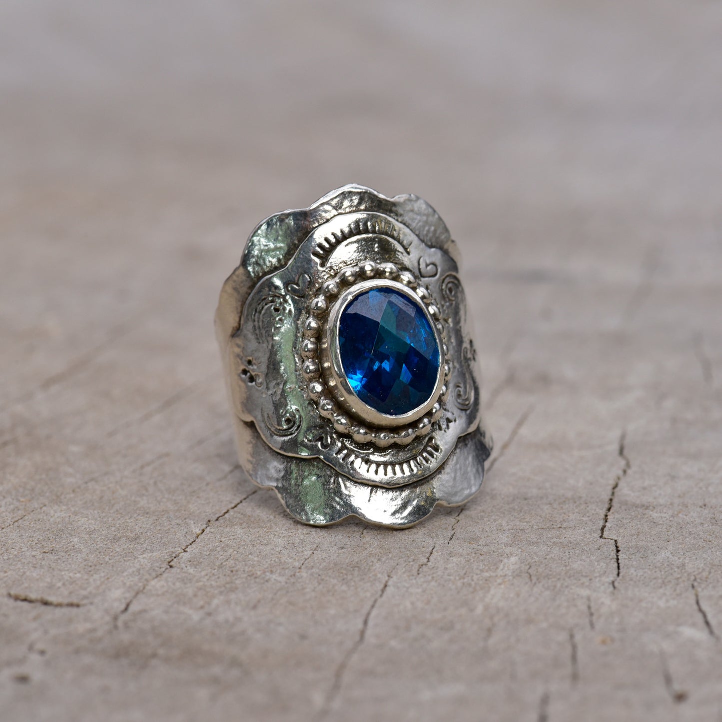 Front of silver ring with a blue gemstone on a textured surface