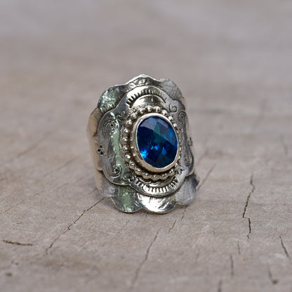 Front of silver ring with a blue gemstone on a textured surface
