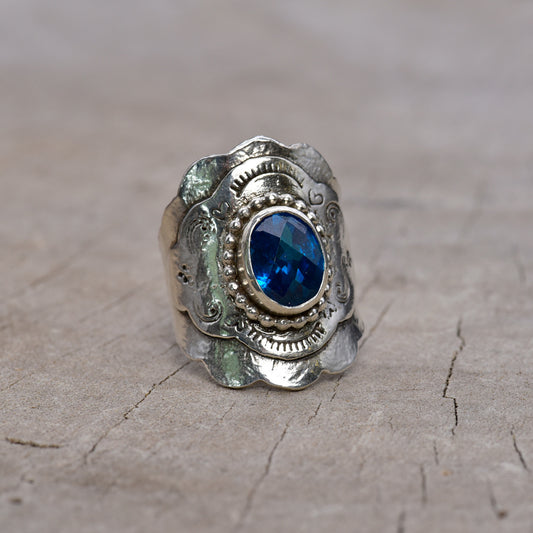 Front of silver ring with a blue gemstone on a textured surface