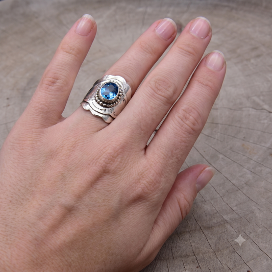 Hand wearing a silver ring with a blue gemstone on a wooden surface