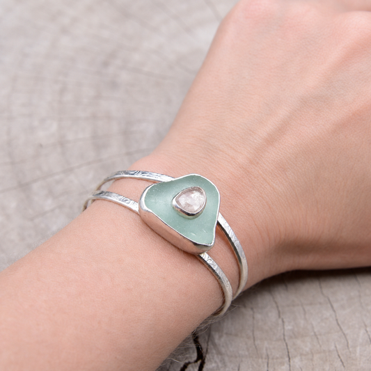 Pale aqua sea glass and pink sapphire cuff bracelet worn on a wrist, showing the double sterling silver bands