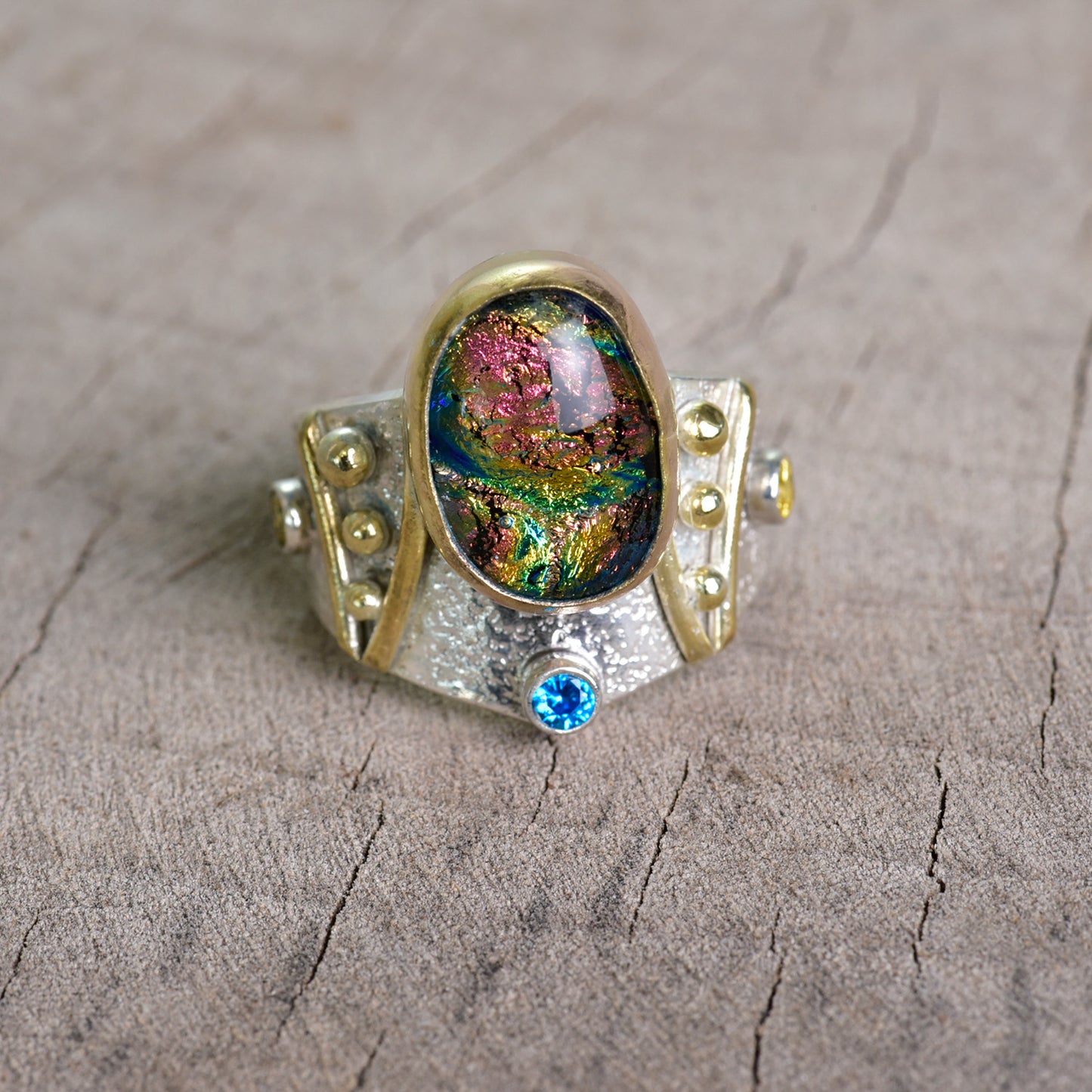 Fused dichroic glass ring in a hand crafted setting of sterling silver with gold accents. (R925)