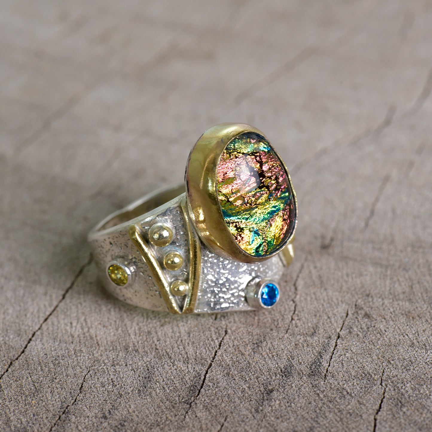 Fused dichroic glass ring in a hand crafted setting of sterling silver with gold accents. (R925)