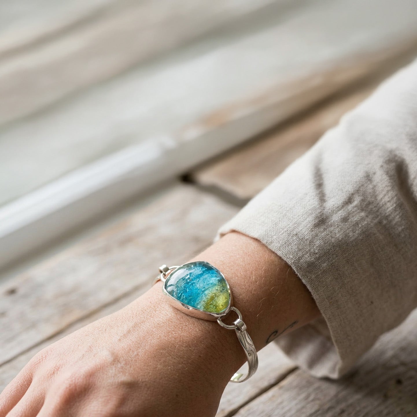 Hand wearing a bracelet with a natural stone design on a wooden surface