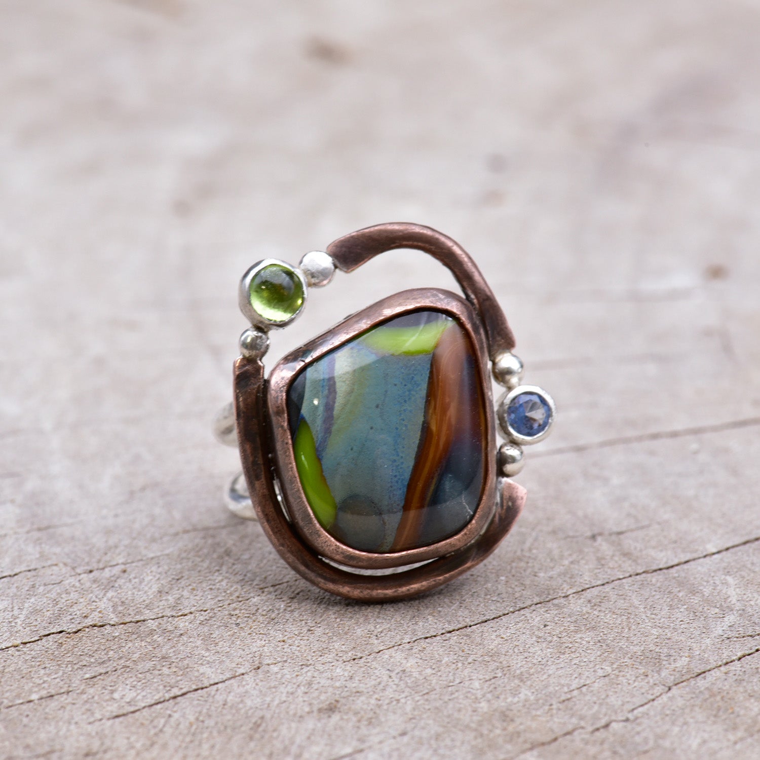 Ring with a colorful stone and embedded gemstones on a textured surface