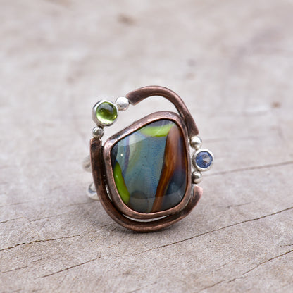 Ring with a colorful stone and embedded gemstones on a textured surface