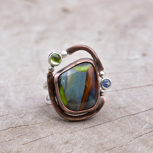 Ring with a colorful stone and embedded gemstones on a textured surface