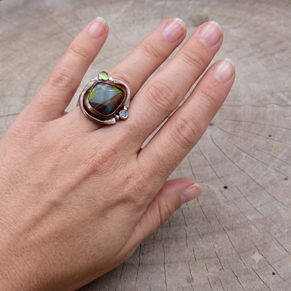 Hand wearing a ring with a colorful stone on a wooden surface