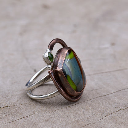 Copper and silver ring with colorful stones on a textured surface.