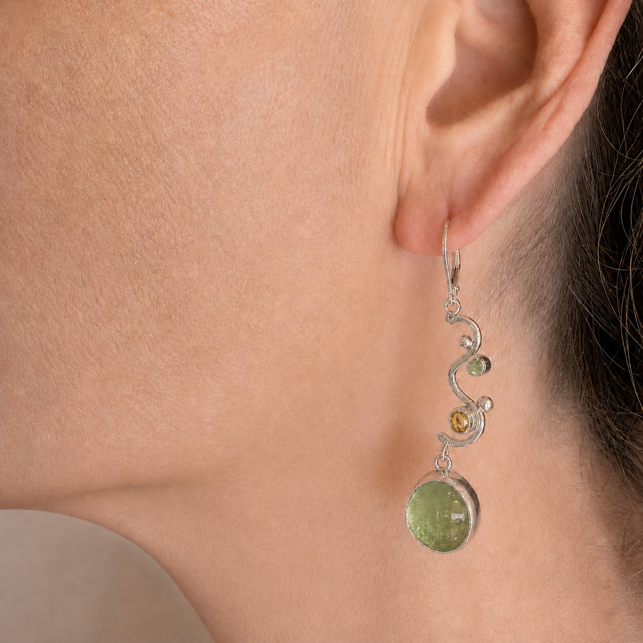 Seafoam green dichroic glass dangle earring worn on the ear, the silver wave dropping the glass just below the jawline