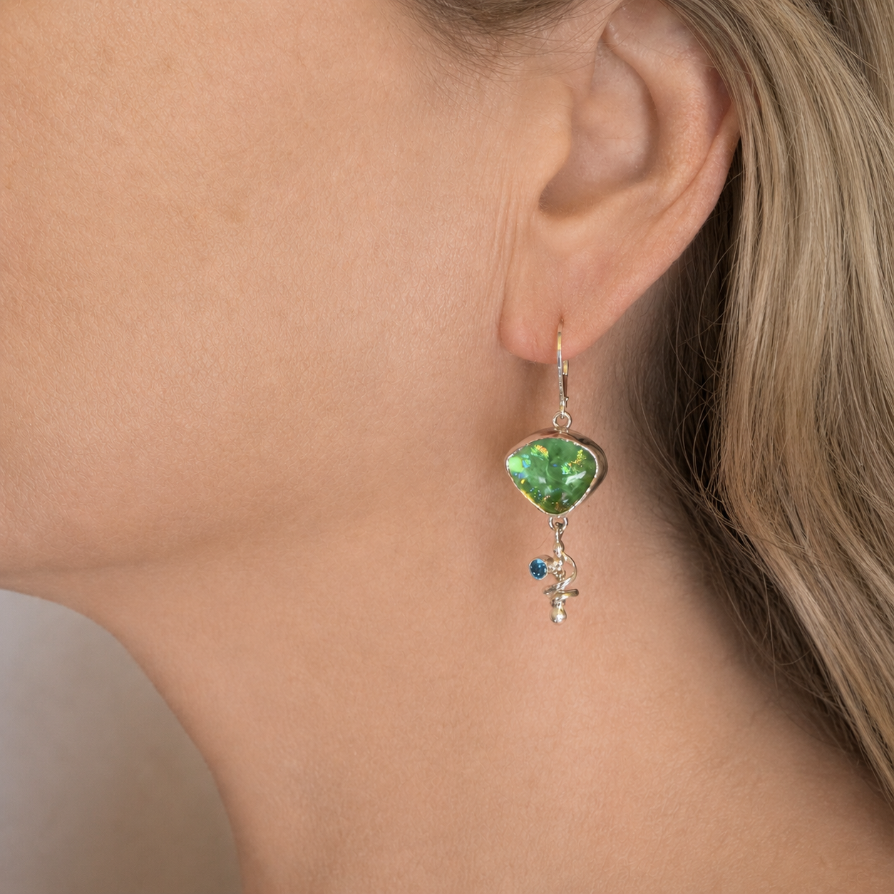 Spring green dichroic glass asymmetric dangle earring worn on the ear, the glass at the top and a silver spiral swinging below