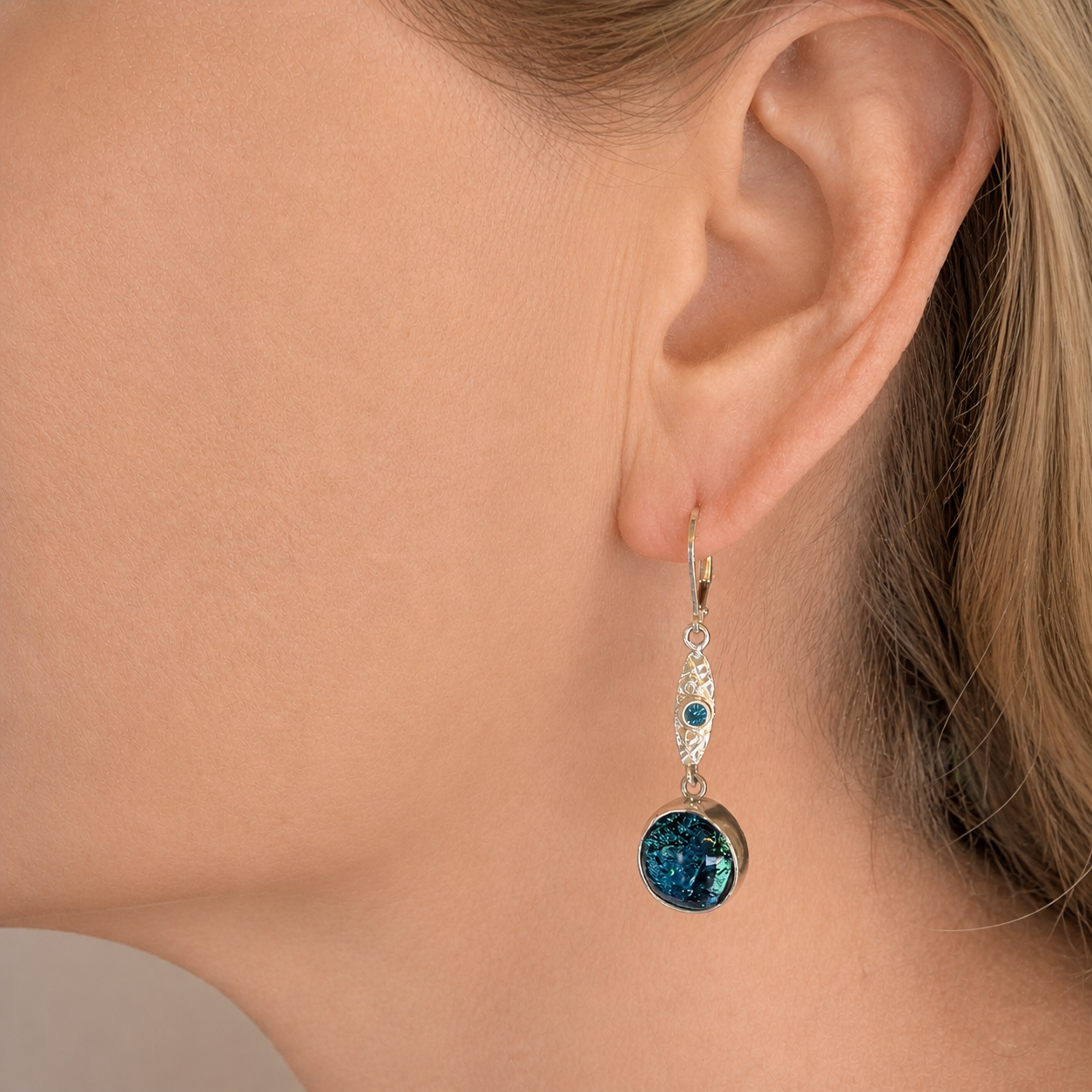 Sapphire blue and turquoise dichroic glass dangle earring worn on the ear, the round cabochon hanging below a textured silver marquise link