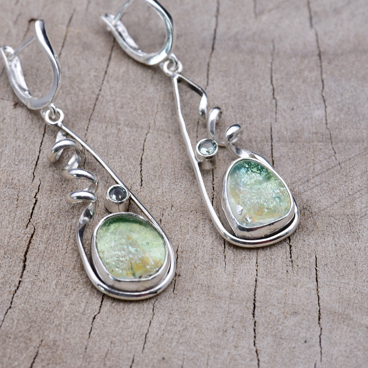 Handmade sea green and aqua dichroic glass dangle earrings in open teardrop Argentium sterling silver frames with corkscrew spirals and aqua cubic zirconia accents, on weathered wood