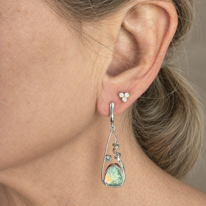 Sea green dichroic glass earring with a silver spiral frame worn on the ear, showing how the long drop hangs