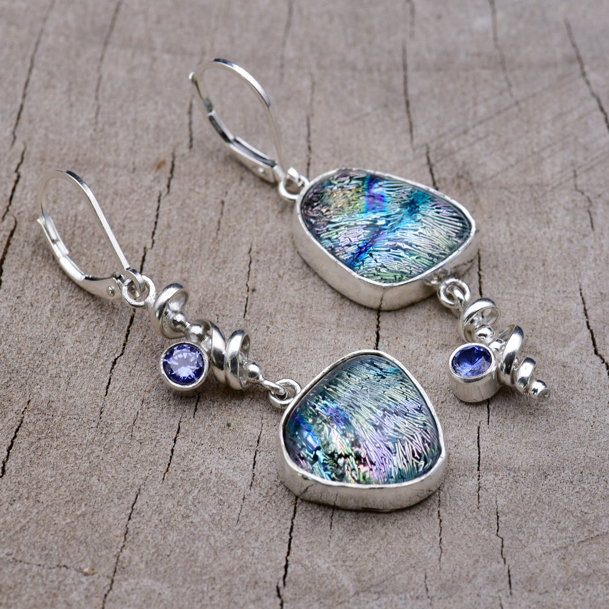 Handmade asymmetric dichroic glass dangle earrings with teal, blue and lavender streaked glass, Argentium sterling silver spiral dangles and violet blue cubic zirconia accents, on weathered wood