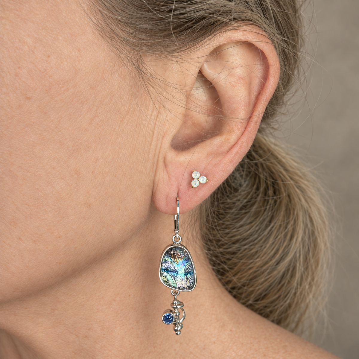 Teal and lavender dichroic glass earring worn on the ear, with the silver spiral and violet blue stone hanging below the glass