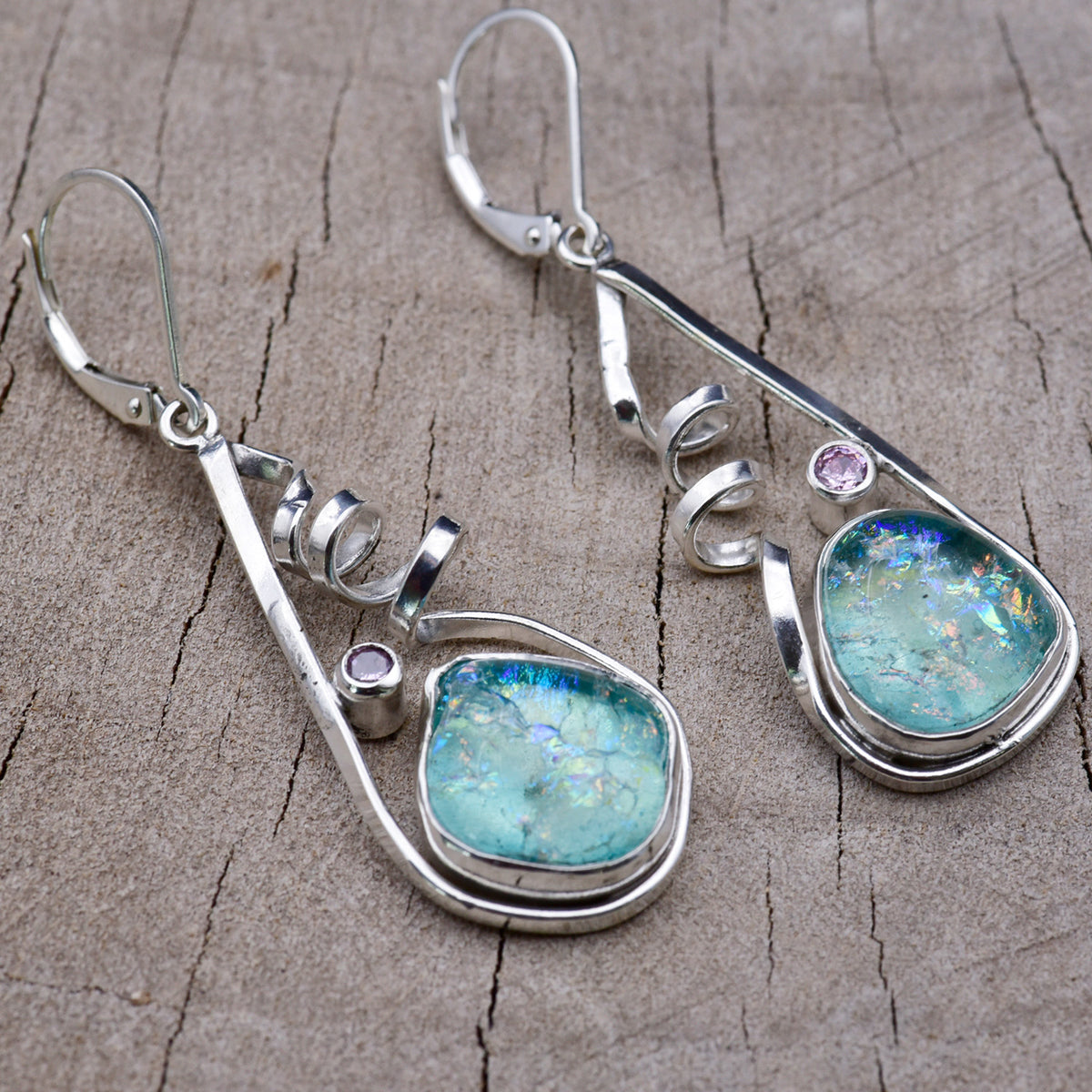 Handmade aqua and turquoise dichroic glass dangle earrings in open teardrop Argentium sterling silver frames with corkscrew spirals and pink cubic zirconia accents, on weathered wood