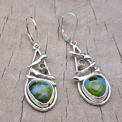 Handmade sky blue and lime green fused glass dangle earrings in open teardrop Argentium sterling silver frames with sculpted branch accents and olive green cubic zirconia, on weathered wood