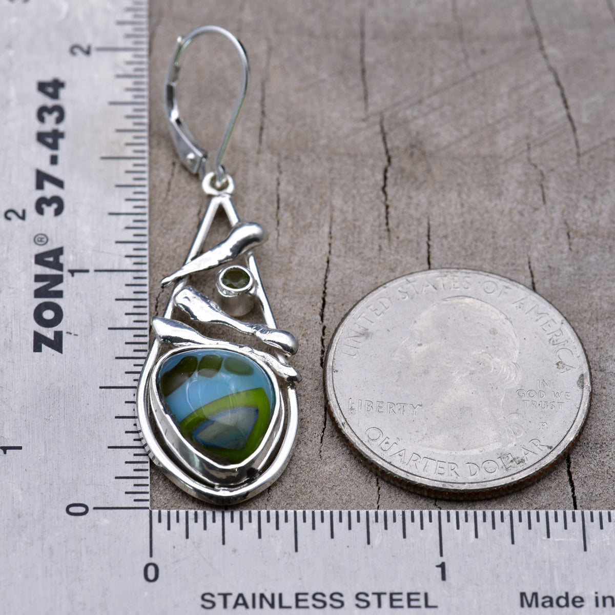 Sky blue and lime green fused glass earring beside a ruler and a quarter for scale, measuring about 2 inches long