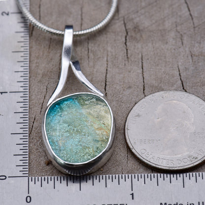Turquoise dichroic glass pendant beside a ruler and a quarter for scale, measuring about 1 3/4 inches tall and 7/8 inch at its widest point.