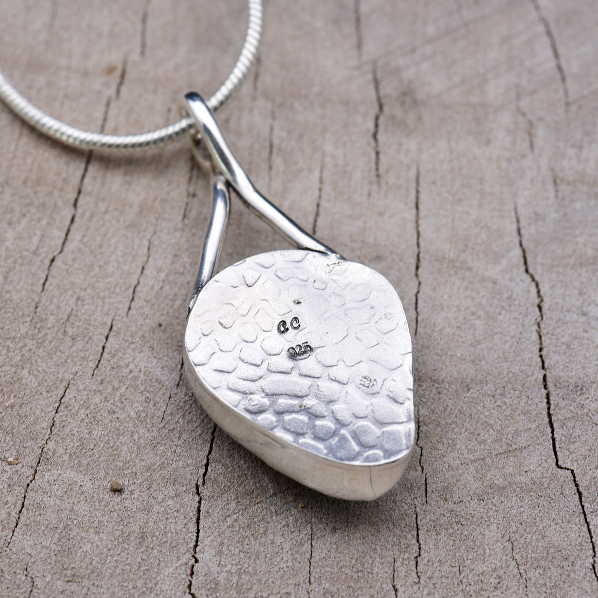Hand-stamped and oxidized silver back of the teardrop pendant, showing the pebbled texture and the CC maker's mark above the 925 hallmark.