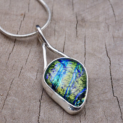Peacock green, cobalt and turquoise dichroic fused glass teardrop pendant set in an Argentium sterling silver bezel with a hand-forged ribbon bail.