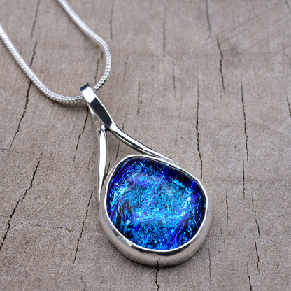 Handmade pendant necklace with an electric blue and aqua dichroic glass cabochon in a sweeping Argentium sterling silver setting, on a silver snake chain.