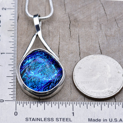 Blue dichroic glass pendant beside a ruler and a quarter for scale, about 2 inches long and 1 inch wide.