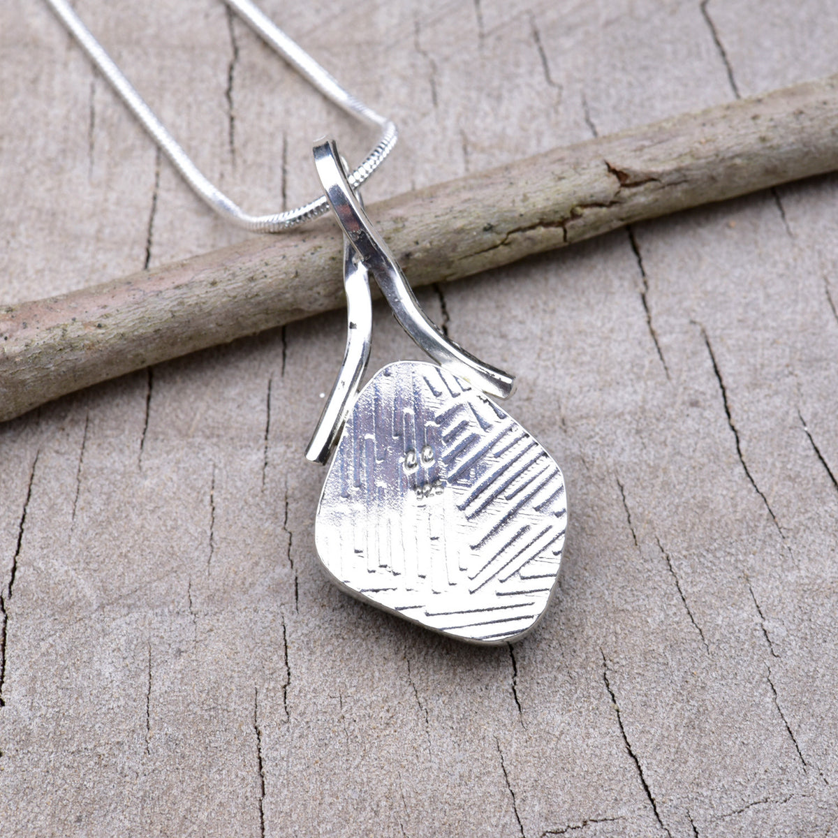 Embossed back of the silver dichroic glass pendant showing the textured Argentium silver and CC maker's mark