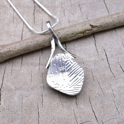Embossed back of the silver dichroic glass pendant showing the textured Argentium silver and CC maker's mark