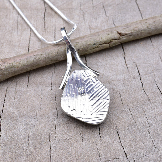 Embossed back of the silver dichroic glass pendant showing the textured Argentium silver and CC maker's mark