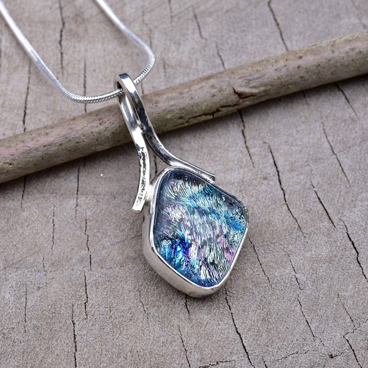 Handmade silver dichroic glass pendant with blue and pink veins in a rounded diamond shape, set in Argentium sterling silver with a ribbon bail, on a snake chain