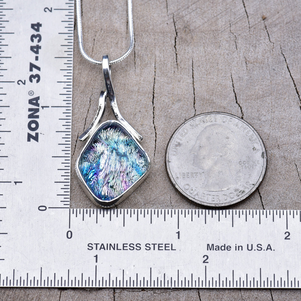 Silver, blue and pink dichroic glass pendant beside a ruler and quarter, about 1½ inches long including the bail