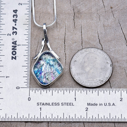 Silver, blue and pink dichroic glass pendant beside a ruler and quarter, about 1½ inches long including the bail