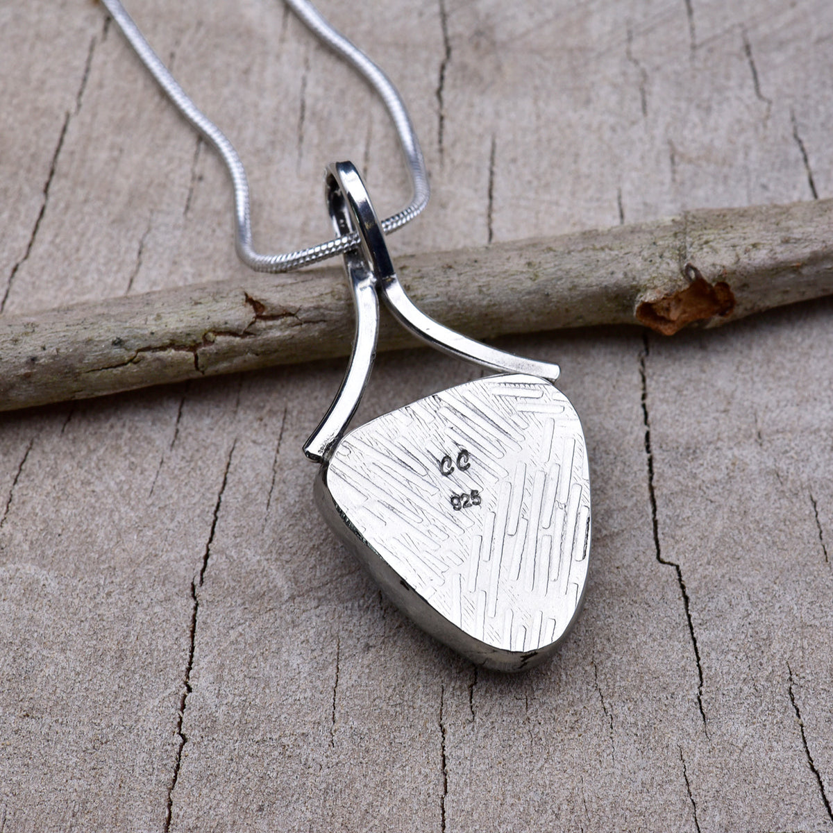Embossed back of the violet triangle dichroic glass pendant showing the textured Argentium silver, CC maker's mark and 925 hallmark