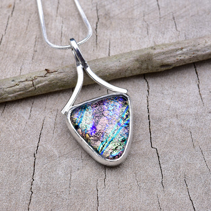 Handmade triangle dichroic glass pendant in violet and pink with blue and green streaks, set in Argentium sterling silver with a ribbon bail, on a snake chain