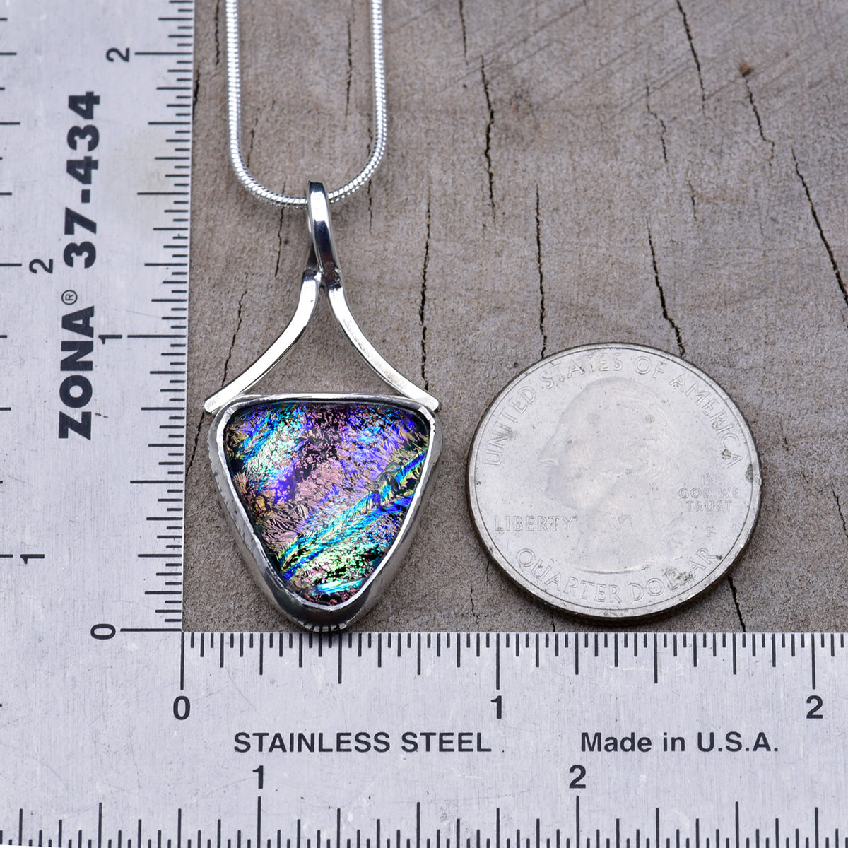 Violet and pink triangle dichroic glass pendant beside a ruler and quarter, about 1½ inches long including the bail