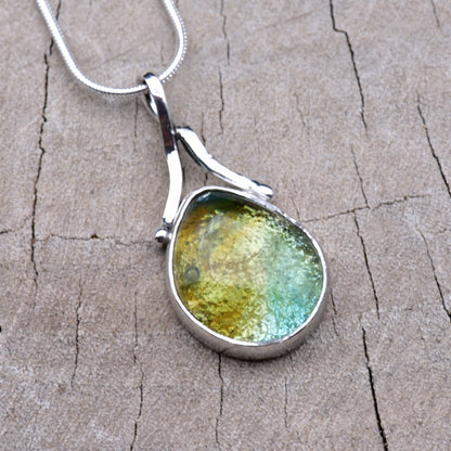 Handmade teardrop dichroic glass pendant in Caribbean gold, green and aqua, set in Argentium sterling silver with a ribbon bail, on a snake chain